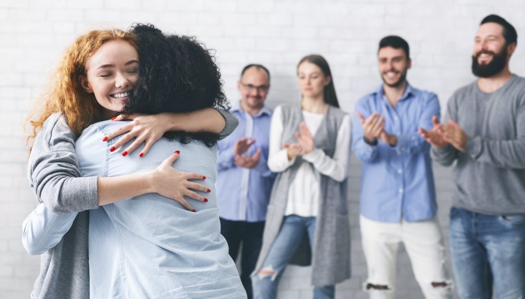 Happy people embracing each other after successful group meeting in rehab